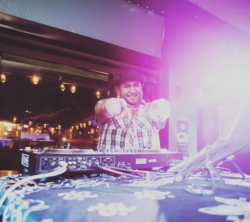 CHIEF grinning and pointing both hands at the camera from behind his Rane controller, stage light flaring purple